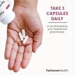 Hand holding three white capsules with bottle tilted above and text that reads: Take 3 capsules daily or as directed by your healthcare practitioner.