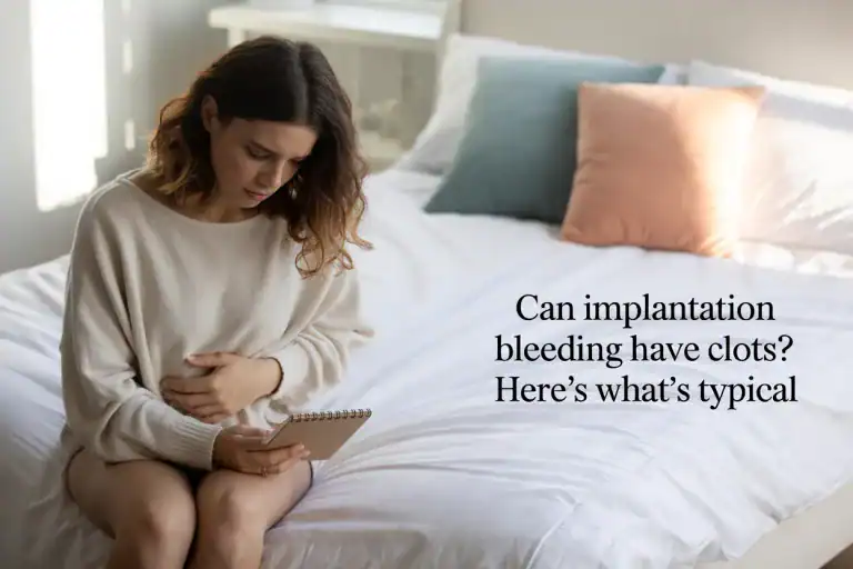Woman sits on a bed holding her lower stomach and notepad, with text: “Can implantation bleeding have clots?”