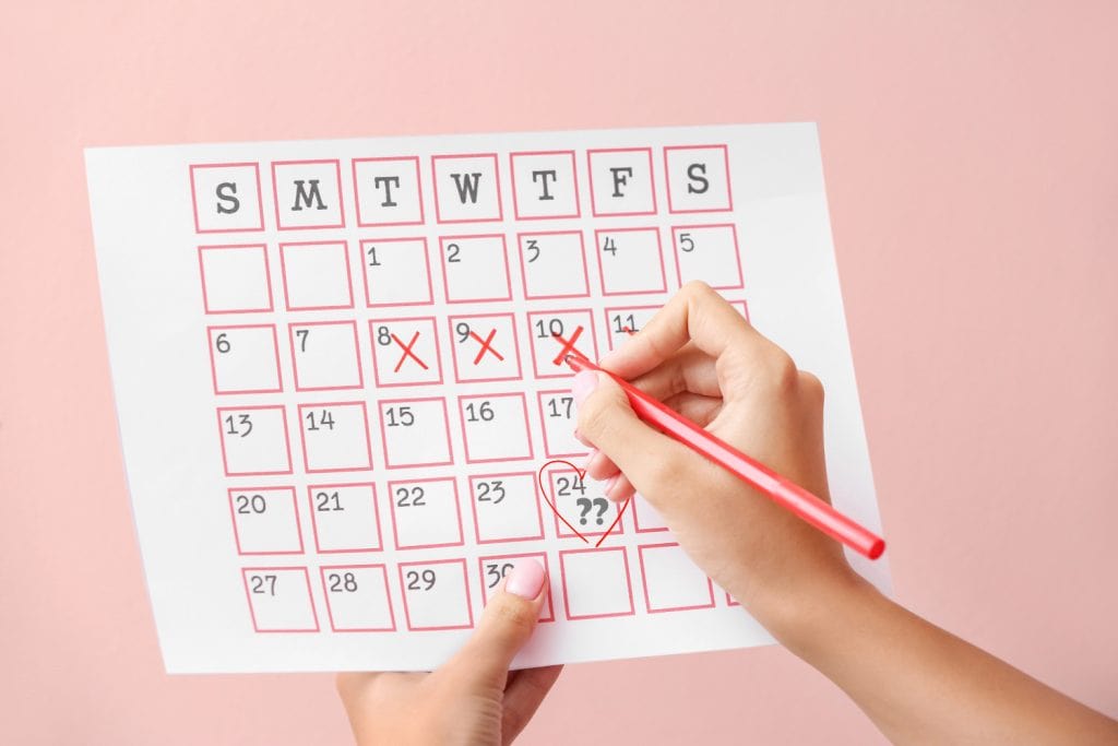 Hand holding a calendar with ovulation dates marked and a question mark in a heart around the test date, symbolizing when to take a pregnancy test